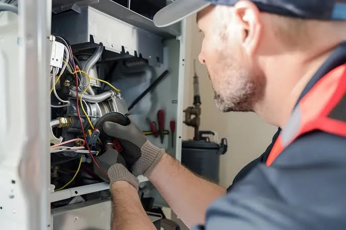 Gloved technician testing wiring inside a heating system